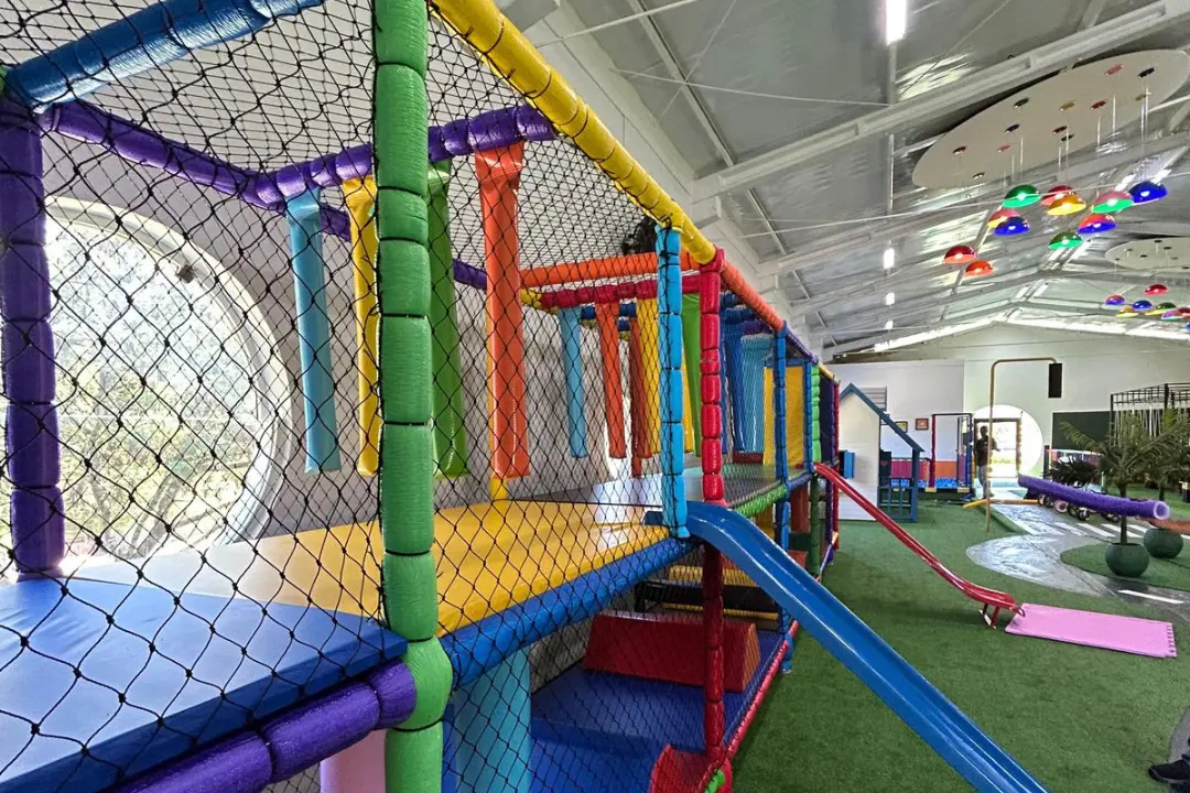 Estrutura de brinquedo infantil colorida em um espaço kids interno, totalmente cercada por rede de proteção preta para a segurança das crianças.