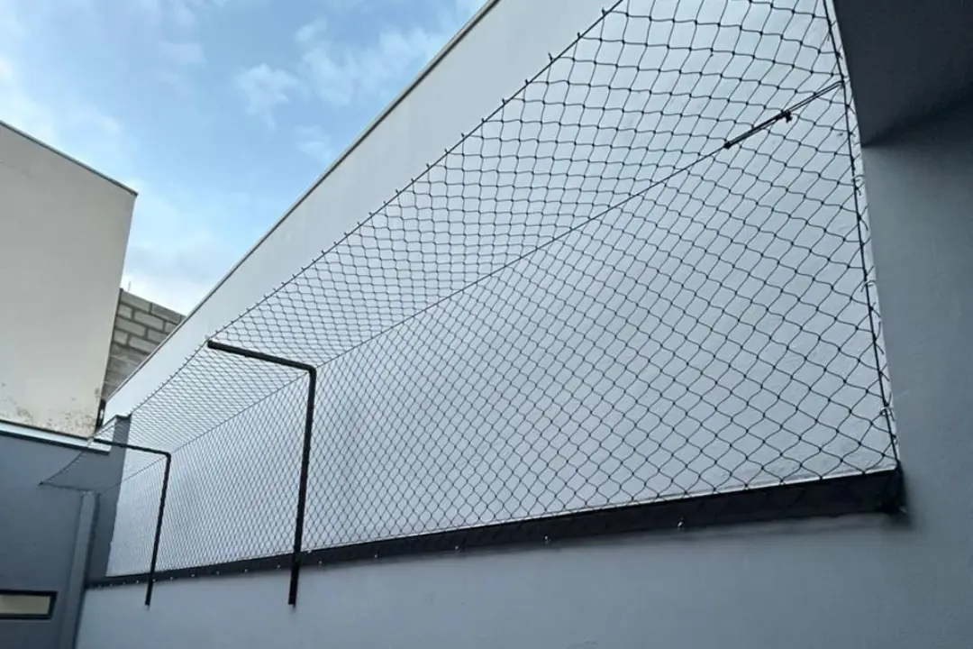 Rede de proteção instalada em uma estrutura metálica preta sobre um muro branco, garantindo a segurança e elevação da barreira no quintal.
