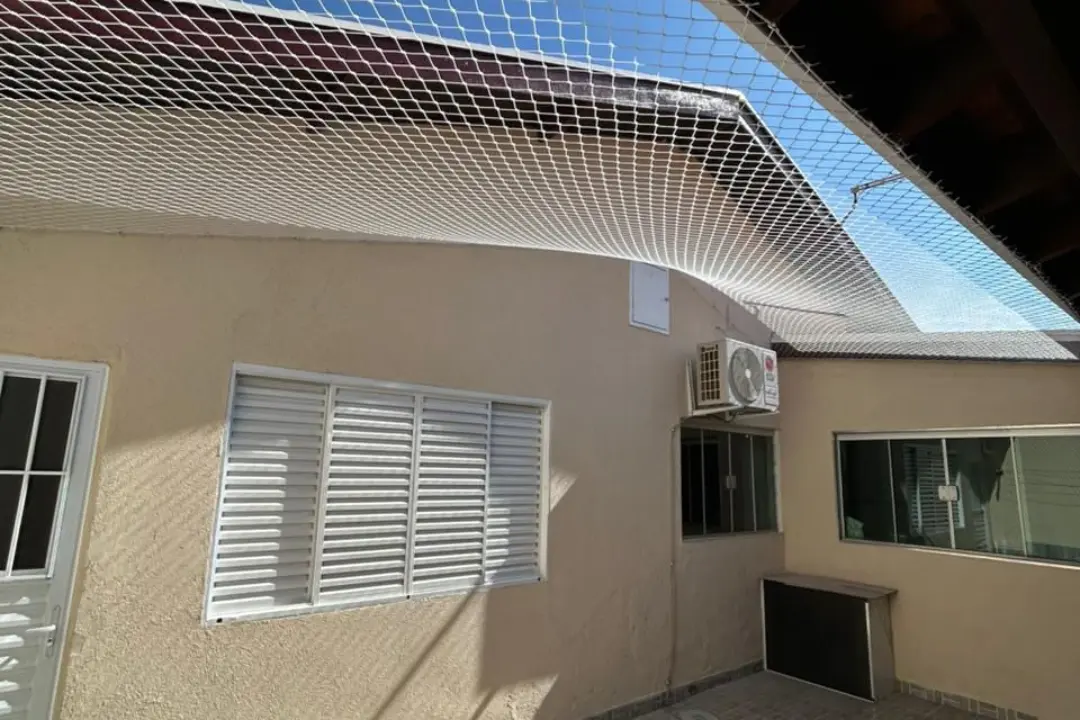 Instalação horizontal de rede de proteção cobrindo a área aberta do quintal de uma casa, fixada nas paredes de forma tensionada e segura.