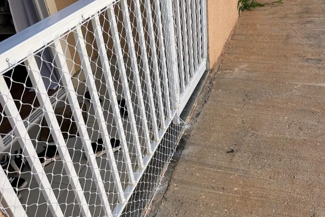 Rede de proteção fixada com abraçadeiras em um portão e grade de metal branco, isolando a área interna da residência de forma segura.