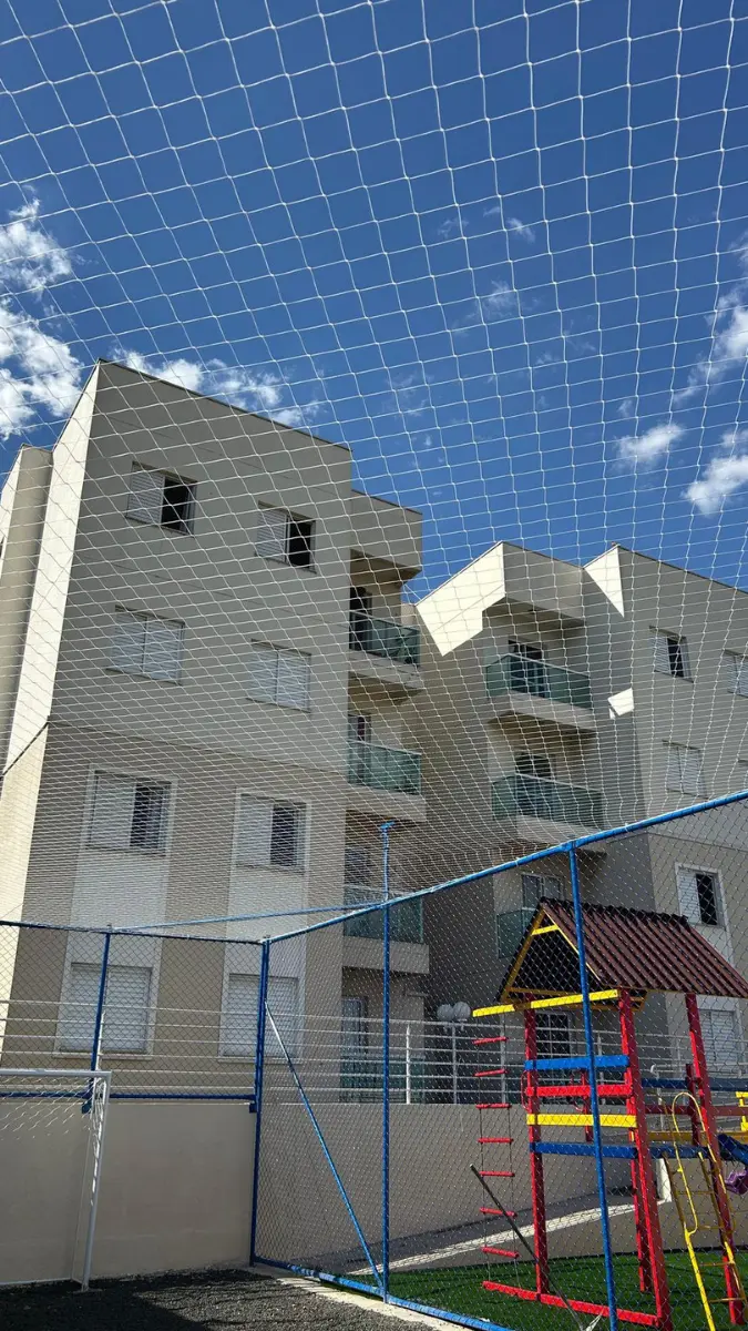 Ampla rede de proteção instalada em uma área de lazer de condomínio com quadra e parquinho infantil, garantindo a segurança do ambiente com os edifícios residenciais ao fundo.