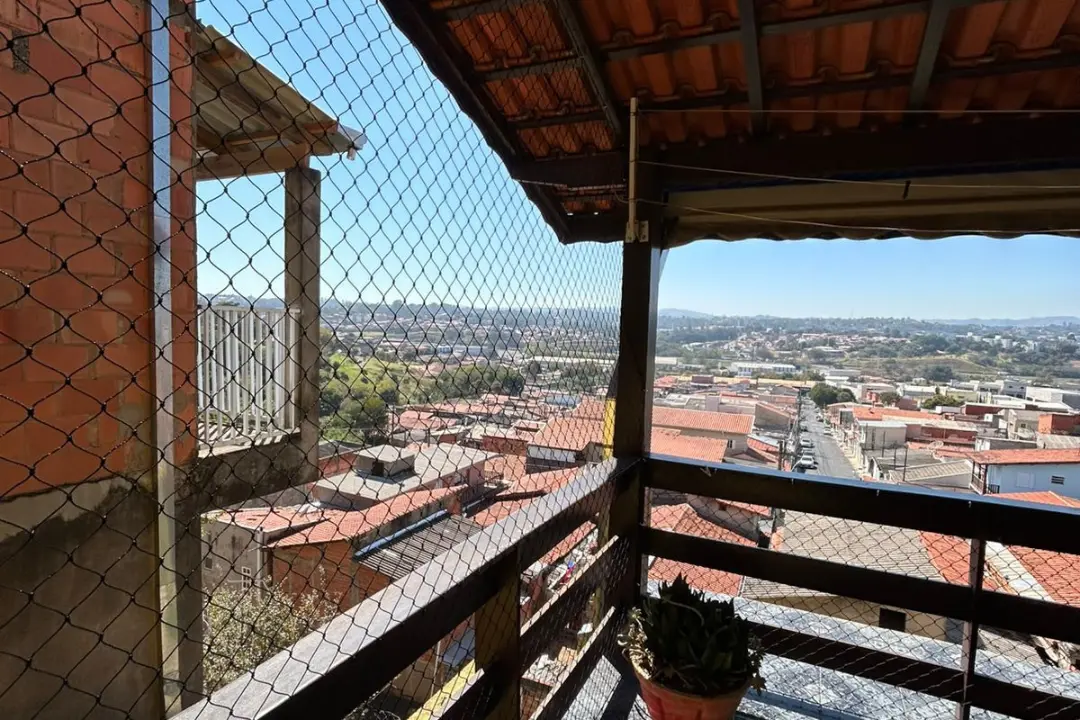 Varanda residencial com telhado aparente e guarda-corpo de madeira, protegida por rede de proteção firme, com vista panorâmica para o bairro.